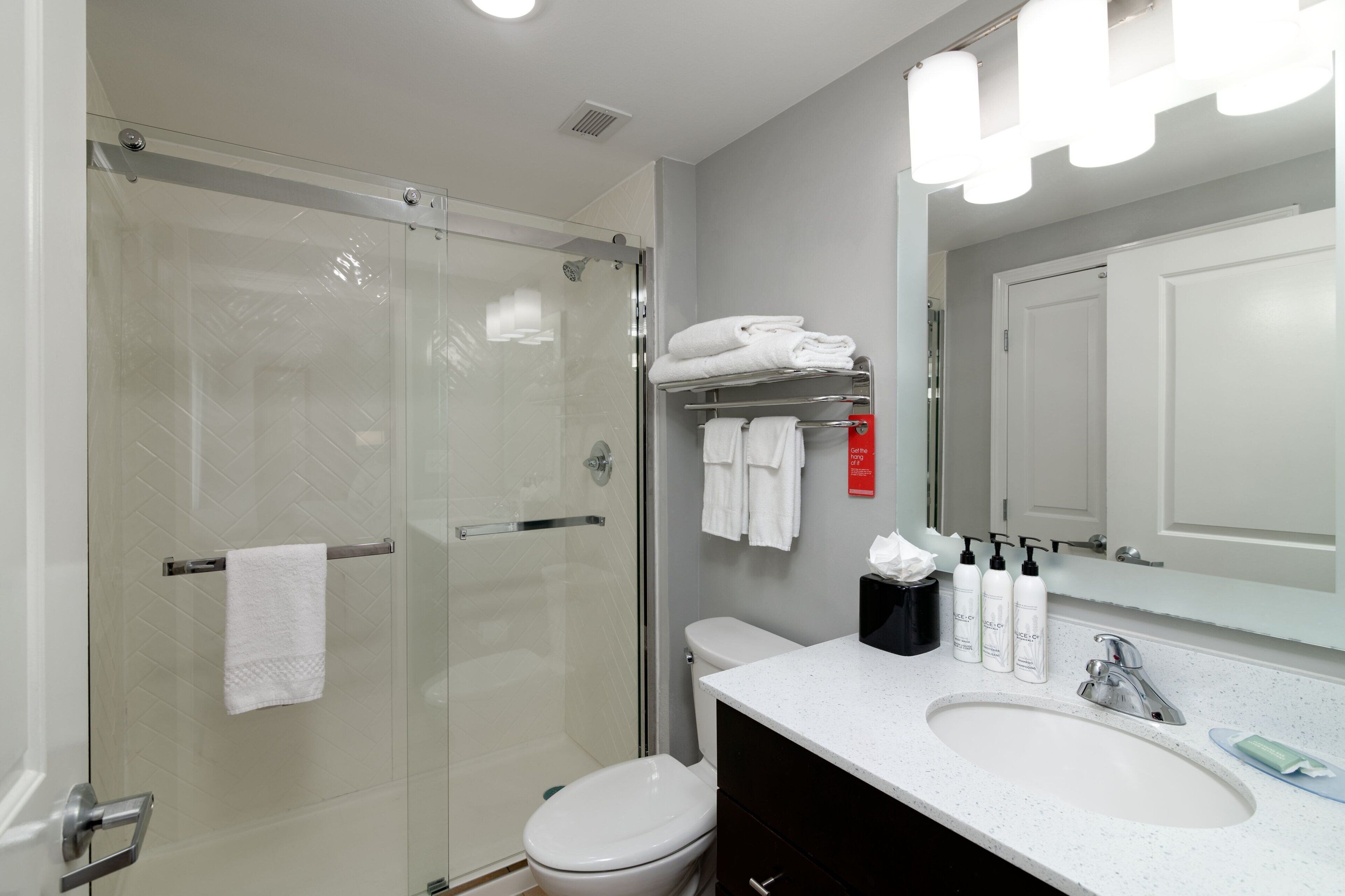 Un baño moderno con ducha acristalada, inodoro blanco y lavamanos con artículos de aseo.