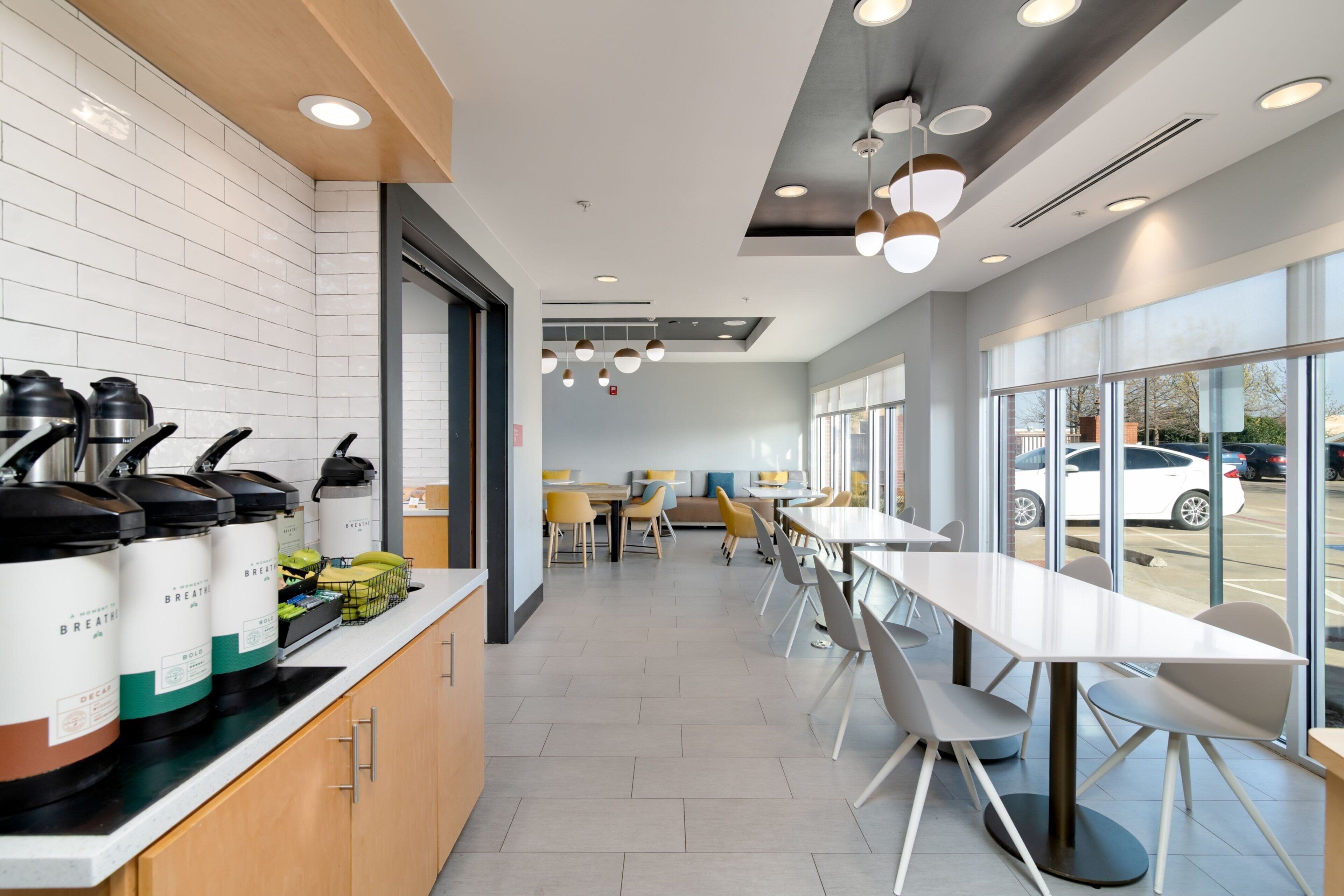 A modern cafe with a long counter, coffee machines, and seating area with tables and chairs.