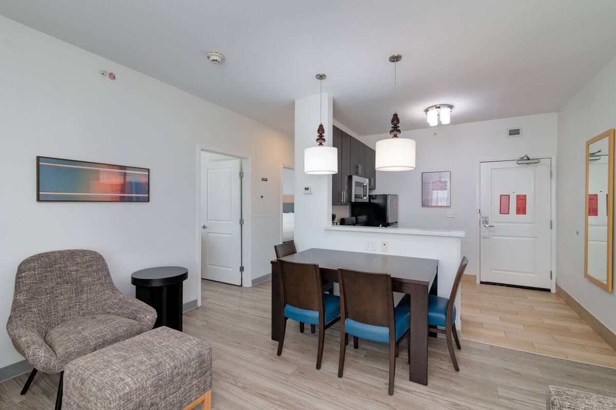 A modern living room with a dining area, a gray armchair, a round table, and a kitchen in the background.