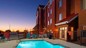 A swimming pool with lounge chairs and a building with a brick facade. - TownePlace Suites Dallas McKinney (McKinney)