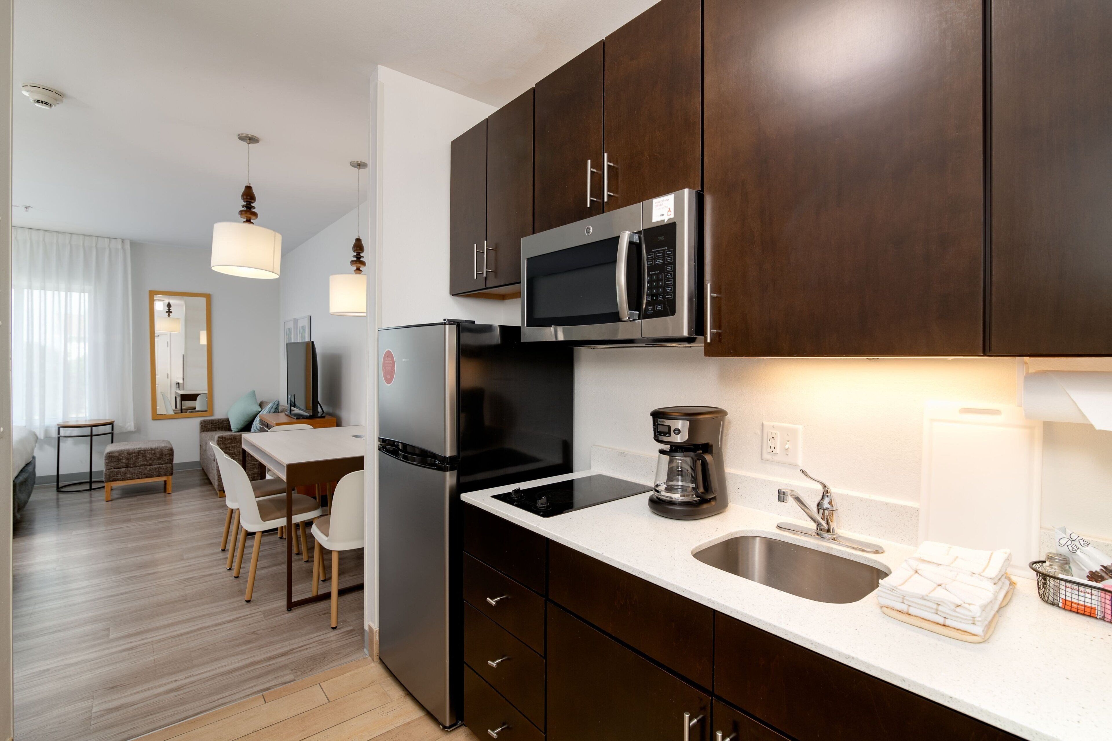 Une cuisine moderne avec des meubles en bois foncé, des appareils électroménagers en acier inoxydable et un plan de travail blanc.