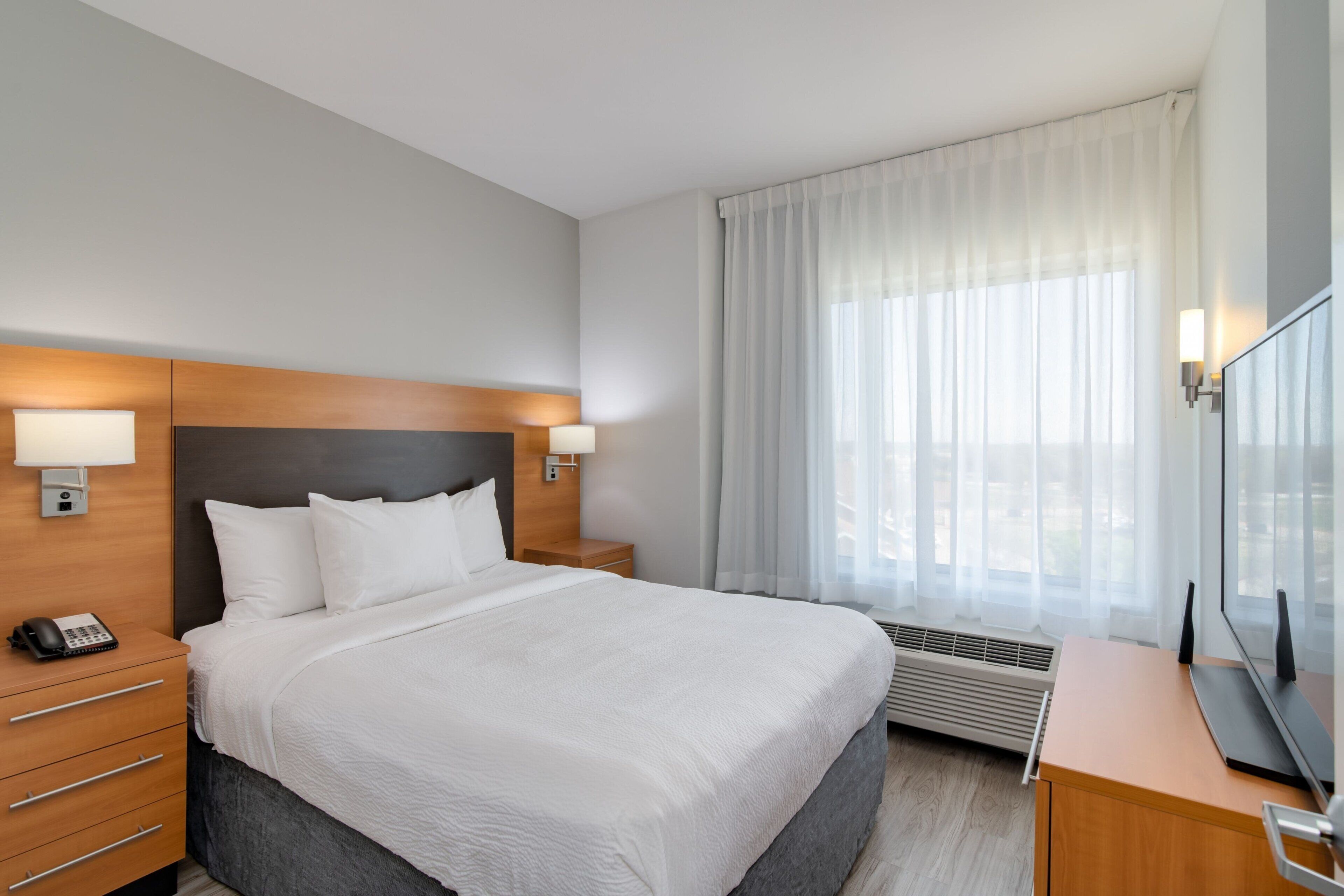 A hotel room with a large bed, bedside lamps, a desk with a computer, a phone, and a TV.