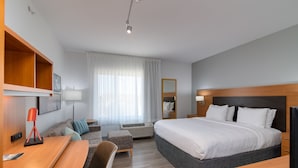 A modern hotel room with a large bed, a desk, a chair, a sofa, and a TV. - TownePlace Suites Dallas McKinney (McKinney)