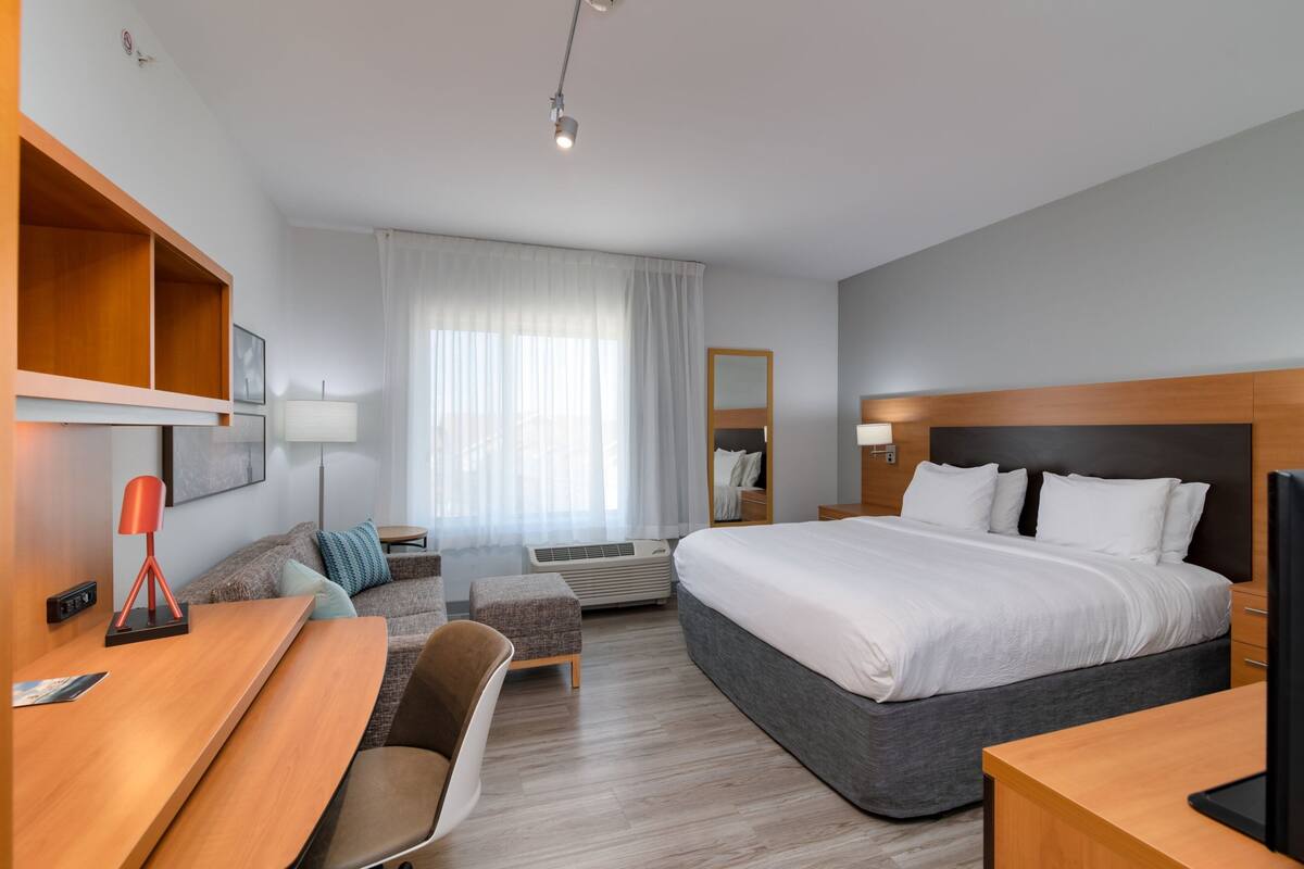 A modern hotel room with a large bed, a desk, a chair, a sofa, and a TV.