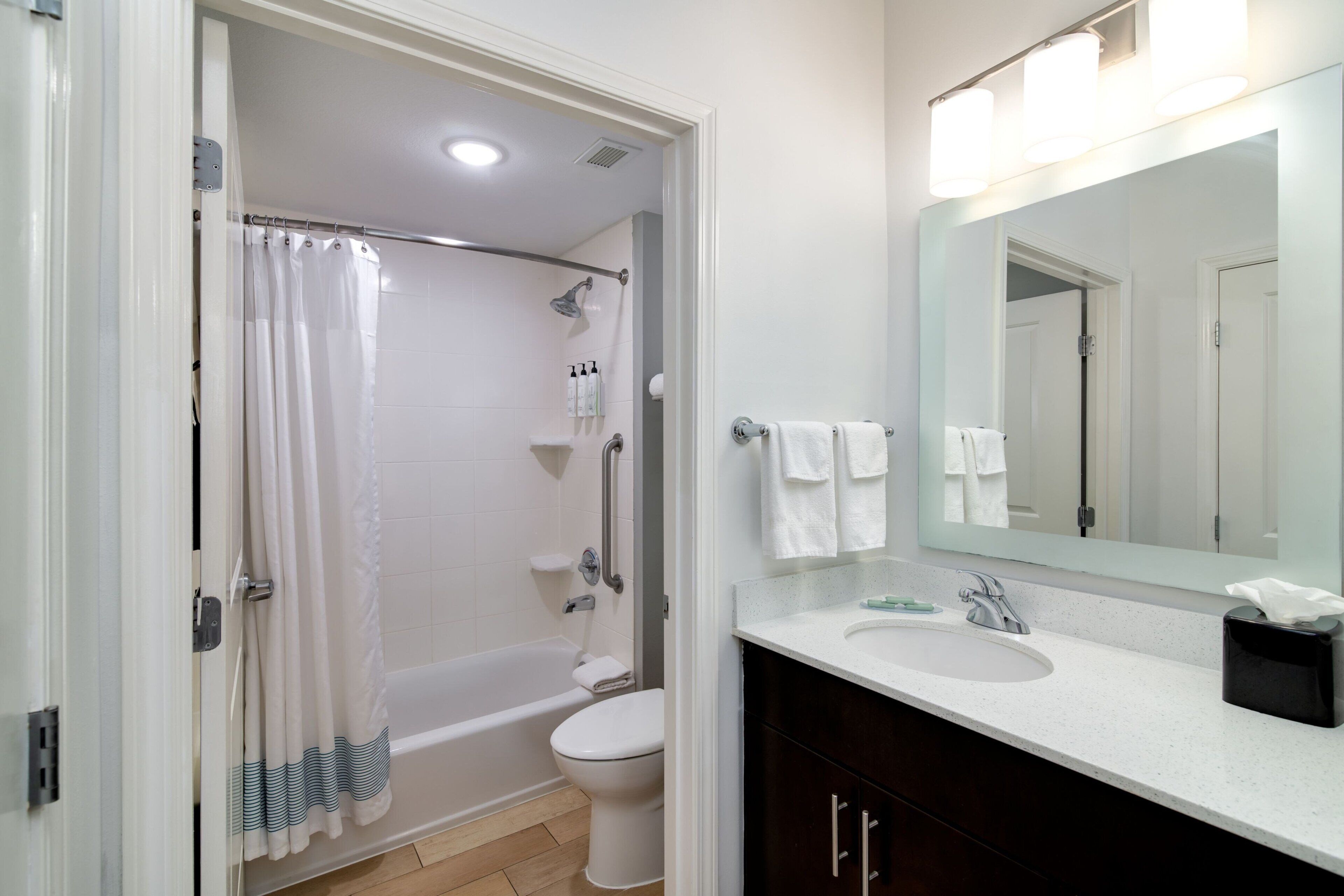 A bathroom with a bathtub, toilet, sink, and a large mirror with lights.