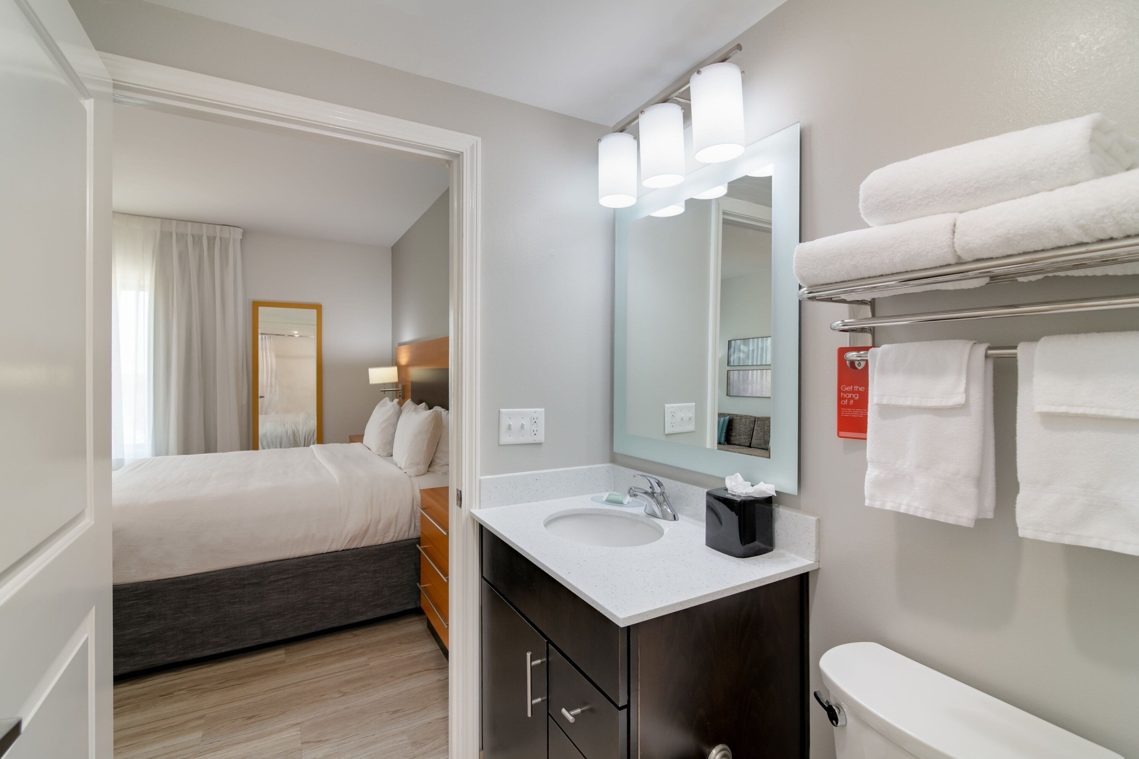 Una habitación de hotel moderna con una cama, un baño con lavamanos, espejo y toallas.