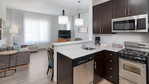 A modern kitchen with a dishwasher, stove, microwave, and a dining area with a sofa and chairs. - TownePlace Suites Dallas McKinney (McKinney)