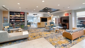 A modern lounge area with seating, a snack bar, and a TV. - TownePlace Suites Dallas McKinney (McKinney)