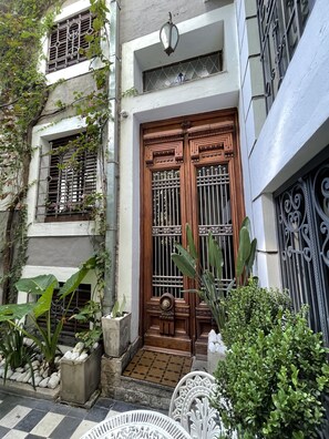 A traditional wooden door with metal bars, a small porch with potted plants, and a tiled entrance.