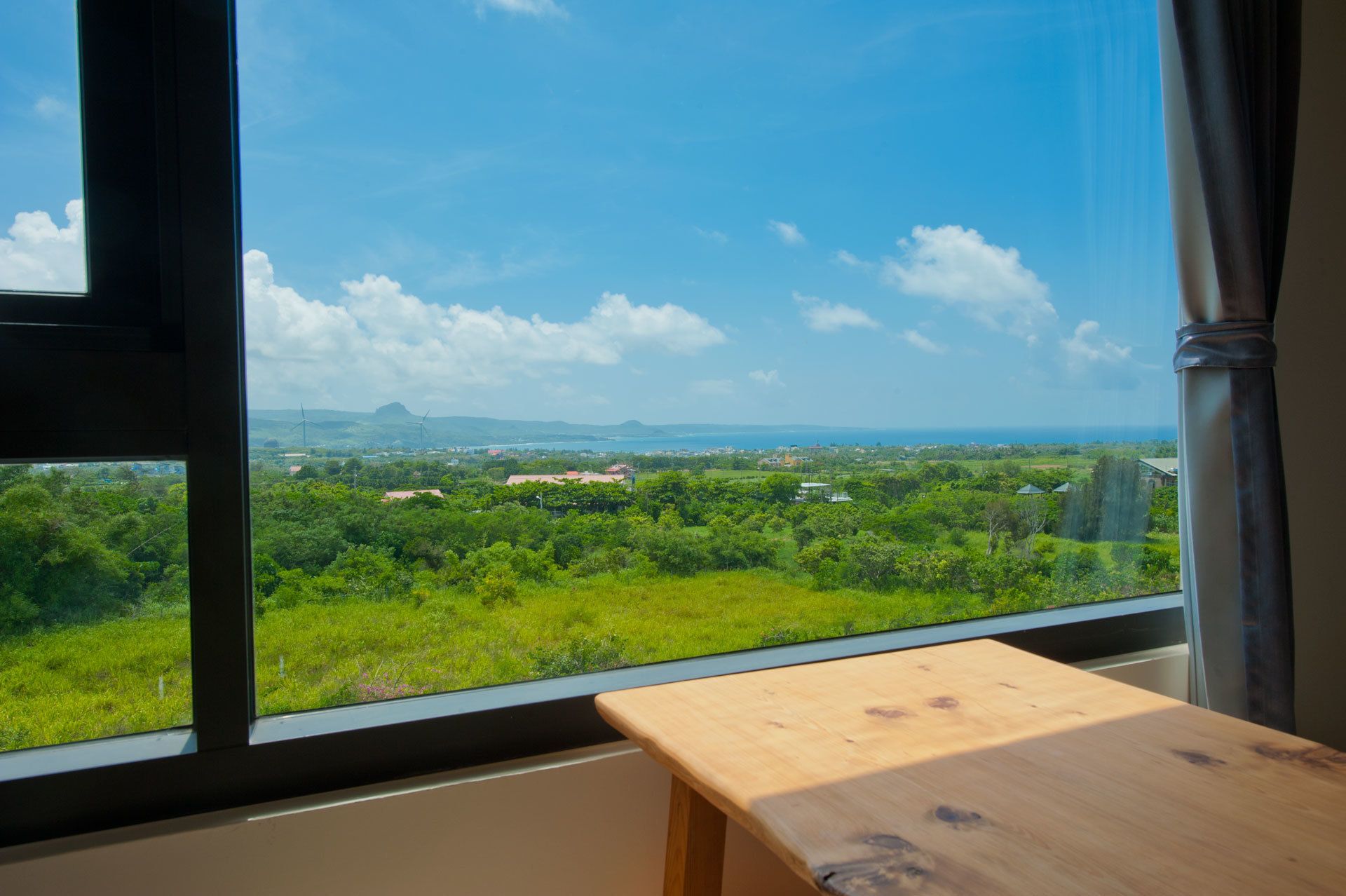 A room with a large window offering a view of a green landscape and distant hills.