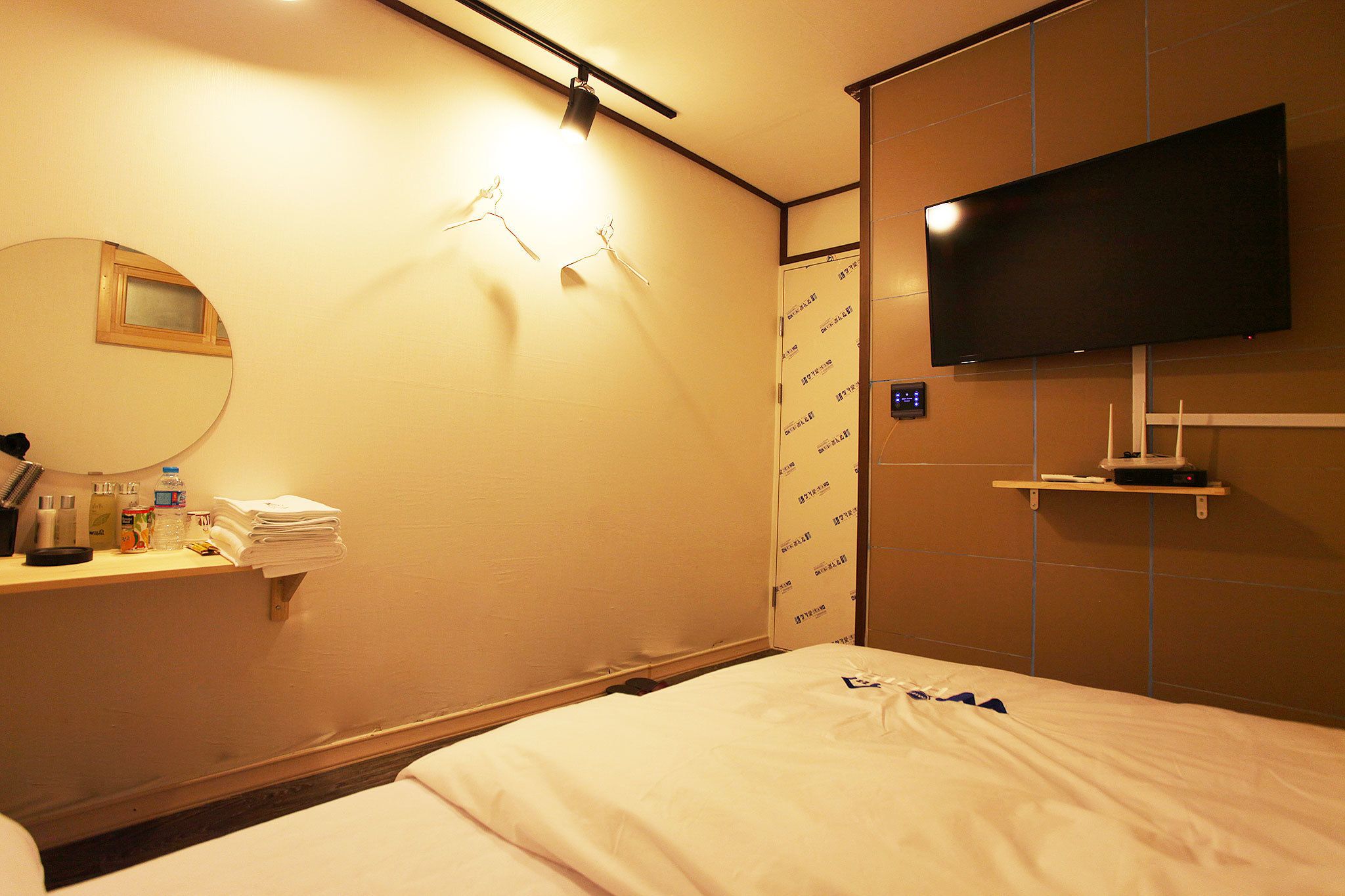 Ein Hotelzimmer mit einem Bett, einem Nachttisch mit Toilettenartikeln, einem an der Wand montierten Fernseher und einem Spiegel.