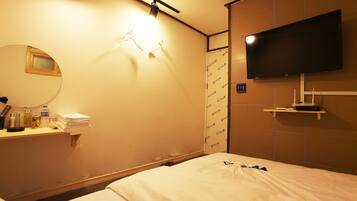 Ein Hotelzimmer mit einem Bett, einem Nachttisch mit Toilettenartikeln, einem an der Wand montierten Fernseher und einem Spiegel.