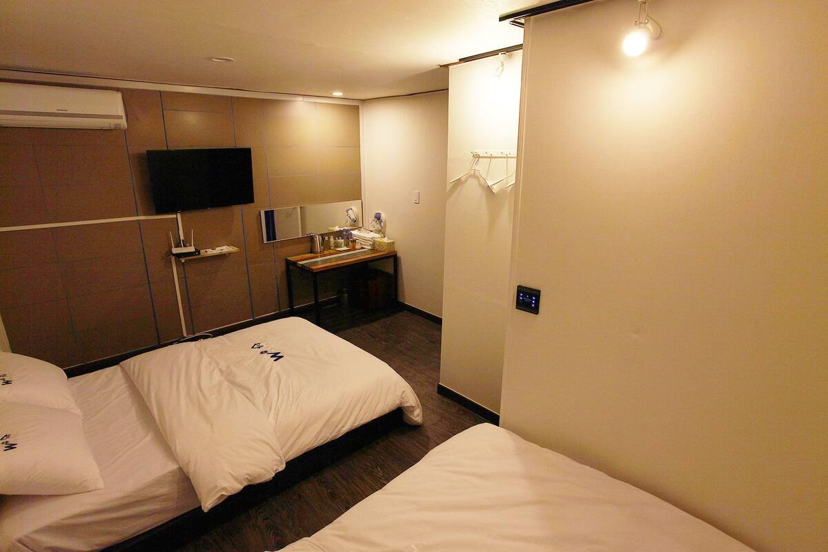 Habitación de hotel con dos camas, un televisor de pantalla plana montado en la pared, una mesita con artículos de aseo y zona de ducha.