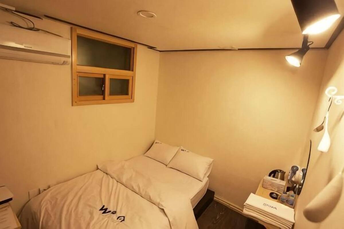 Un dormitorio pequeño y bien iluminado con una cama individual, una ventana y una mesita de noche con artículos de aseo.