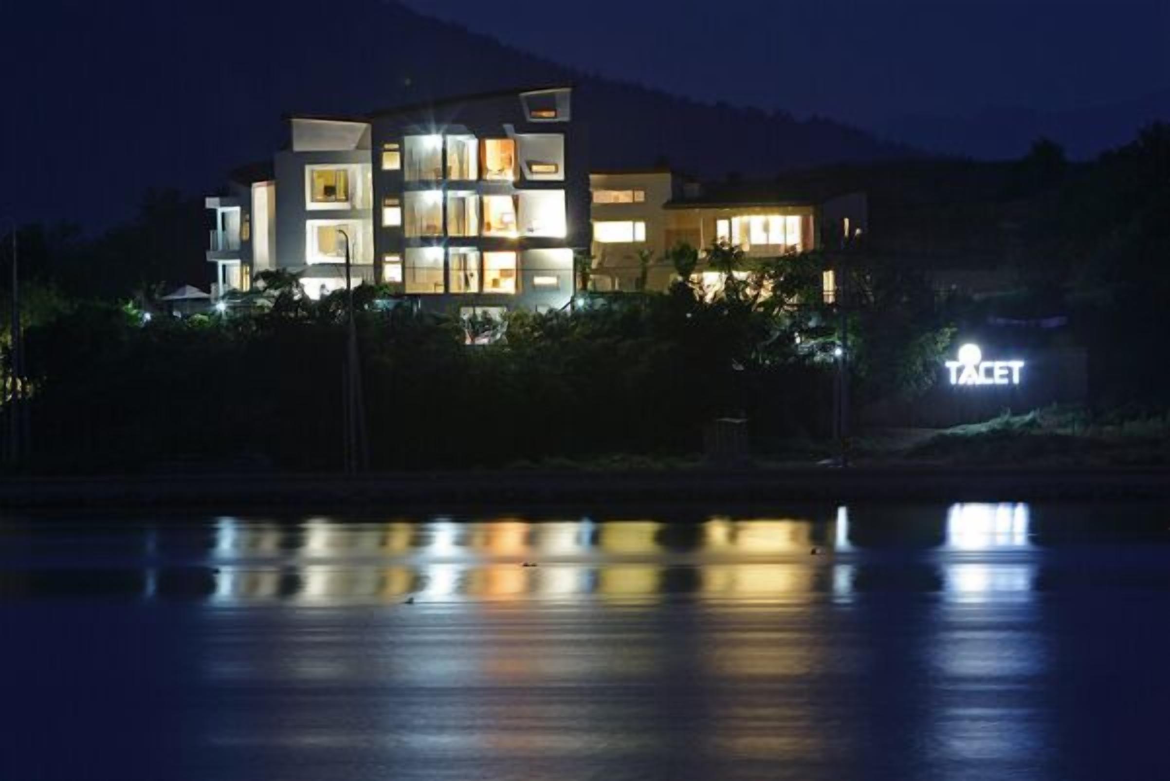 Un hotel moderno de varios pisos con ventanas iluminadas y una señalización visible que dice "TACET".