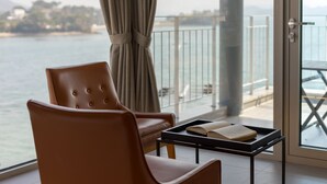 A room with a view of the sea, a brown leather chair, a small table with a tray holding a book, and a curtain tied back. - Tacet Pension (Tongyeong)