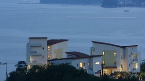 A coastal building with multiple floors and balconies, overlooking a calm sea with a distant island. - Tacet Pension (Tongyeong)