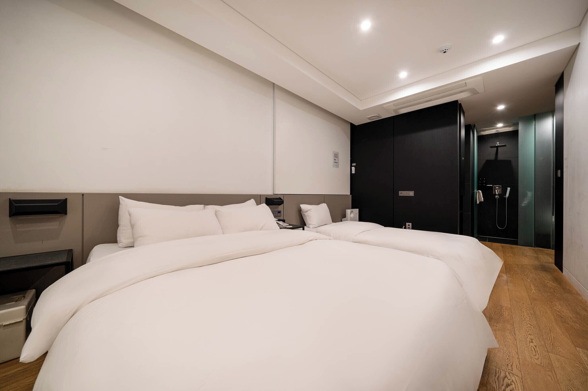 A modern hotel room with a large bed, a dark wardrobe, and a shower area.