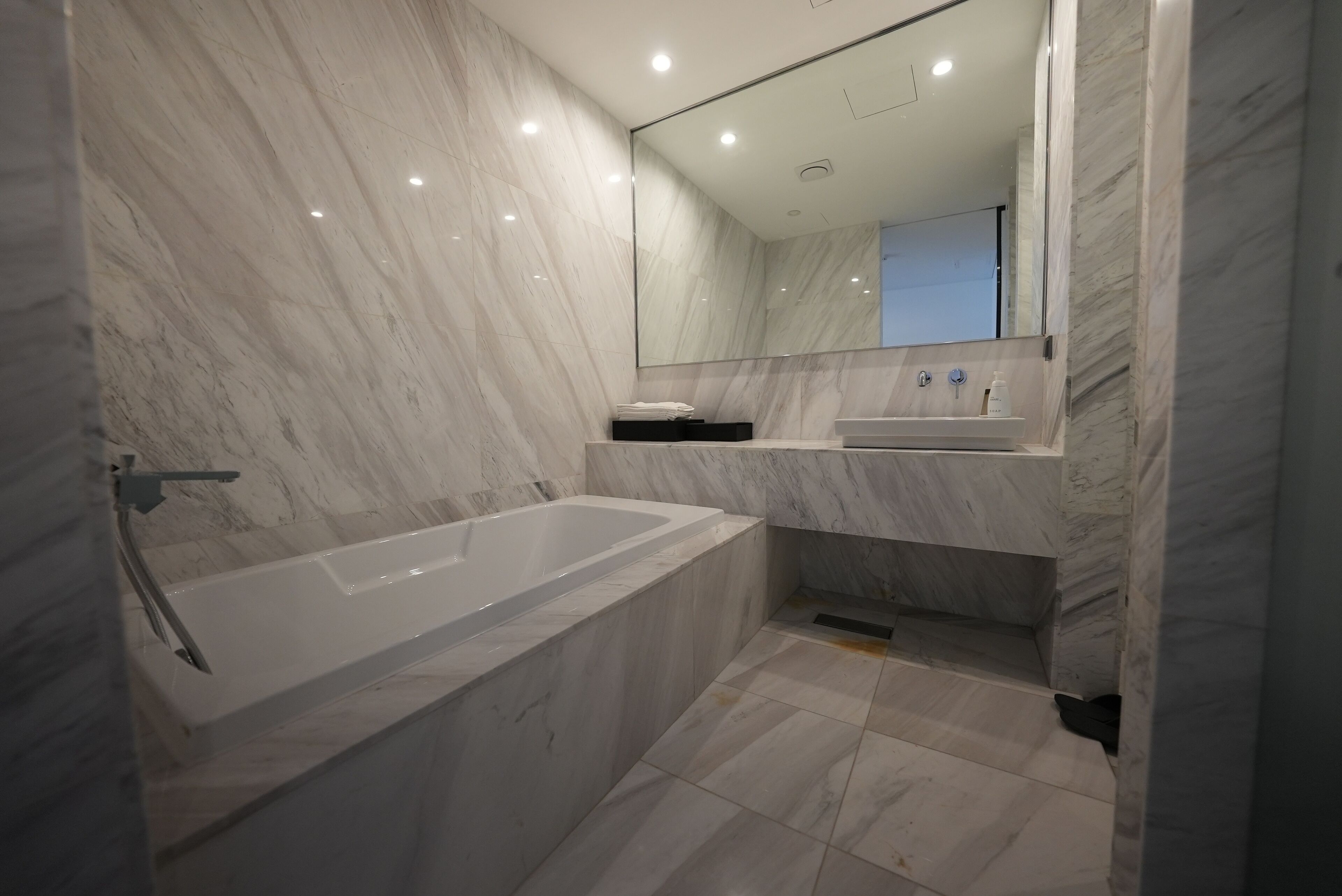 Un baño moderno con piso de mármol, una bañera grande, un lavamanos y un espejo.