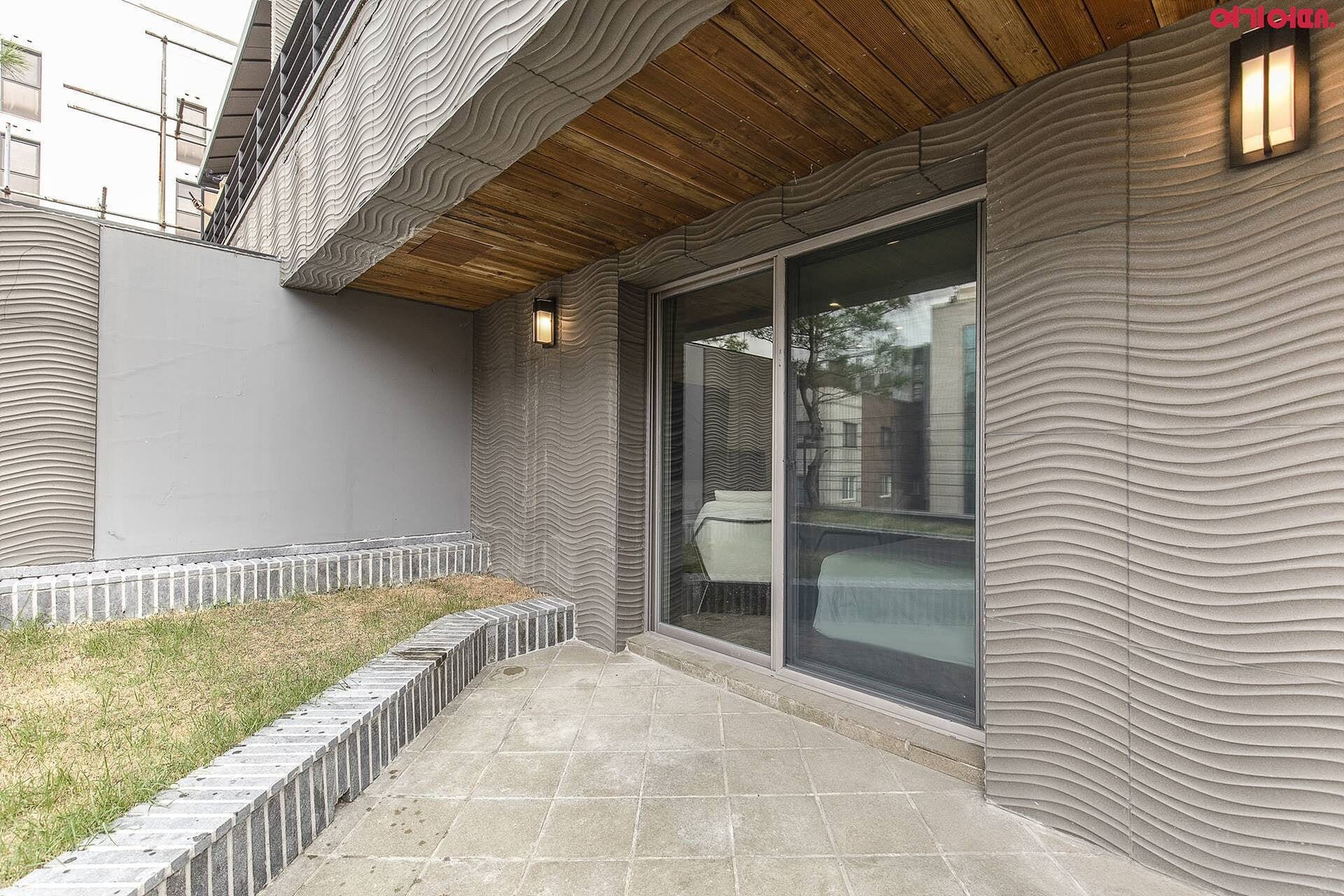 A modern building with a unique wavy facade, a covered patio area, and a large sliding glass door.