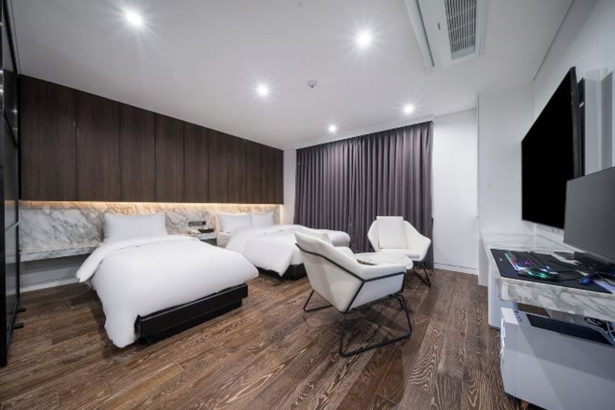 A modern hotel room with a large bed, a sofa, a chair, and a desk with a computer.