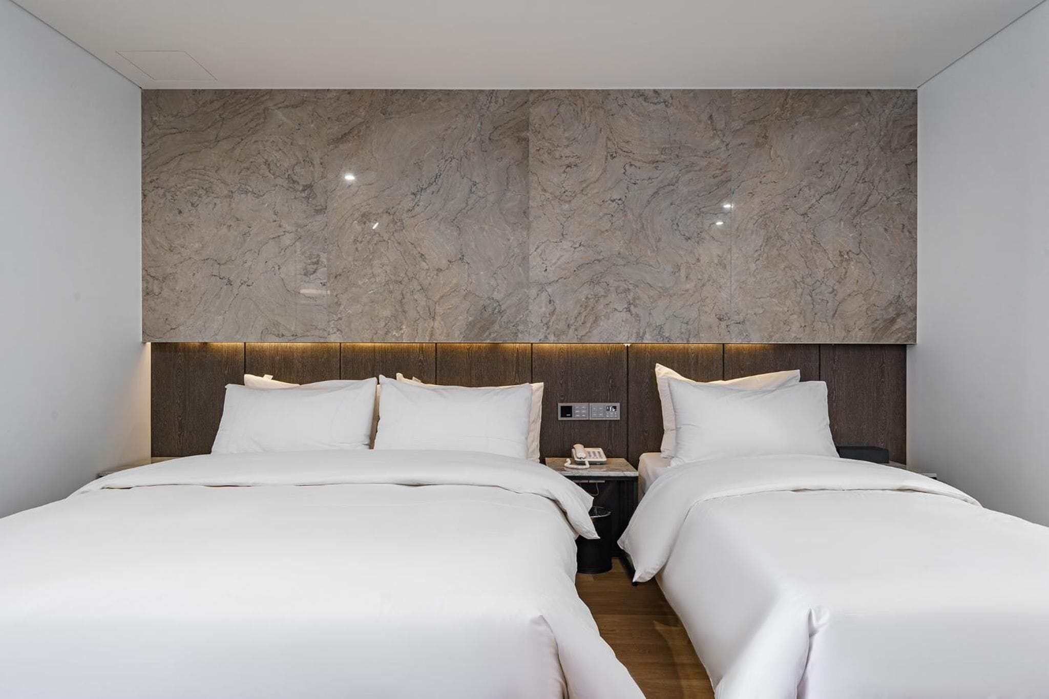 A modern hotel room with two beds, marble headboard, and a small bedside table with a phone.
