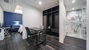 Una habitación moderna con suelo de madera oscura, una mesa de comedor con sillas, una pared azul de acento, un armario negro y un box de ducha de vidrio.
