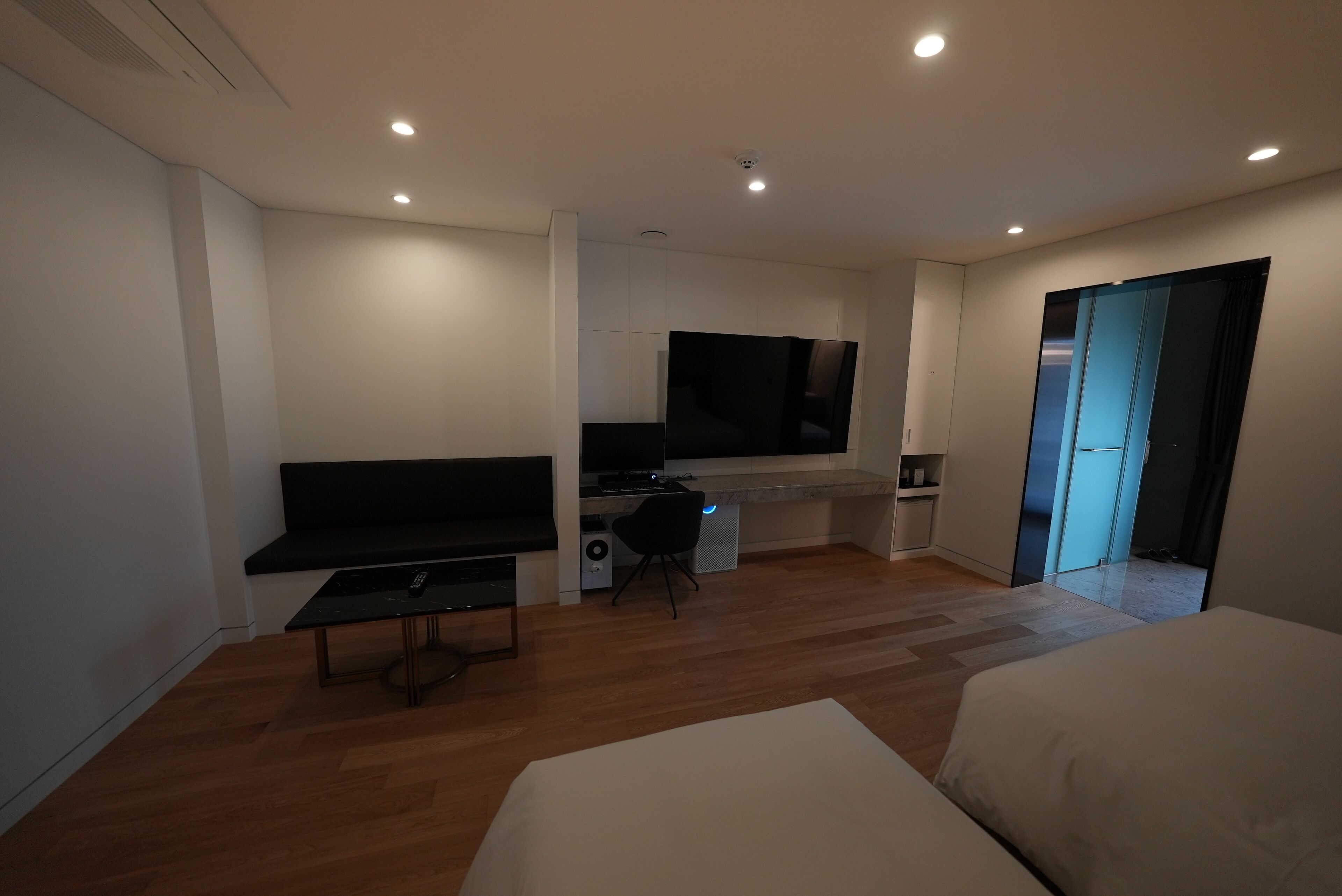 Ein modernes Hotelzimmer mit einem großen Bett, einem Schreibtisch mit Computer, einem Fernseher und einer Schiebetür zu einem Badezimmer.