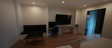 Ein modernes Hotelzimmer mit einem großen Bett, einem Schreibtisch mit Computer, einem Fernseher und einer Schiebetür zu einem Badezimmer.