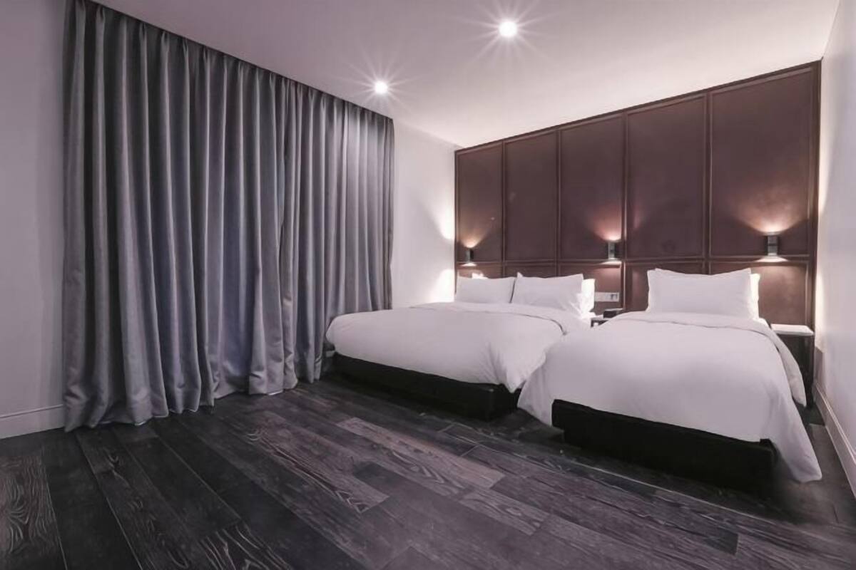Ein Schlafzimmer mit zwei Betten, dunklem Holzboden und einem großen Fenster mit Vorhängen.