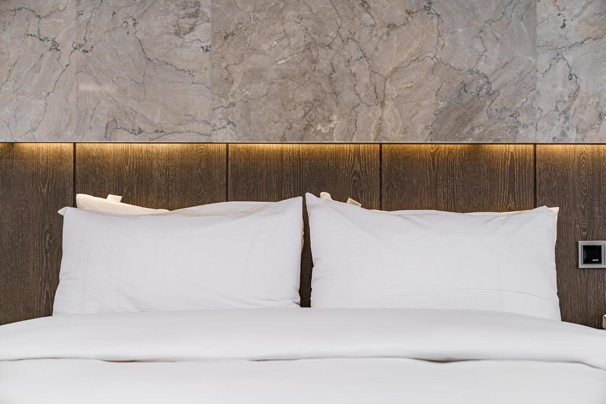A bed with white bedding, a wooden headboard, and a marble-patterned wall.
