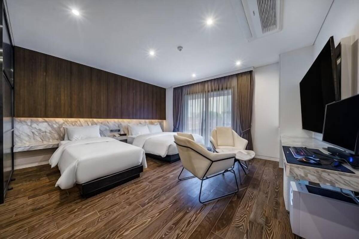 A modern hotel room with two beds, a desk, a chair, and a TV.