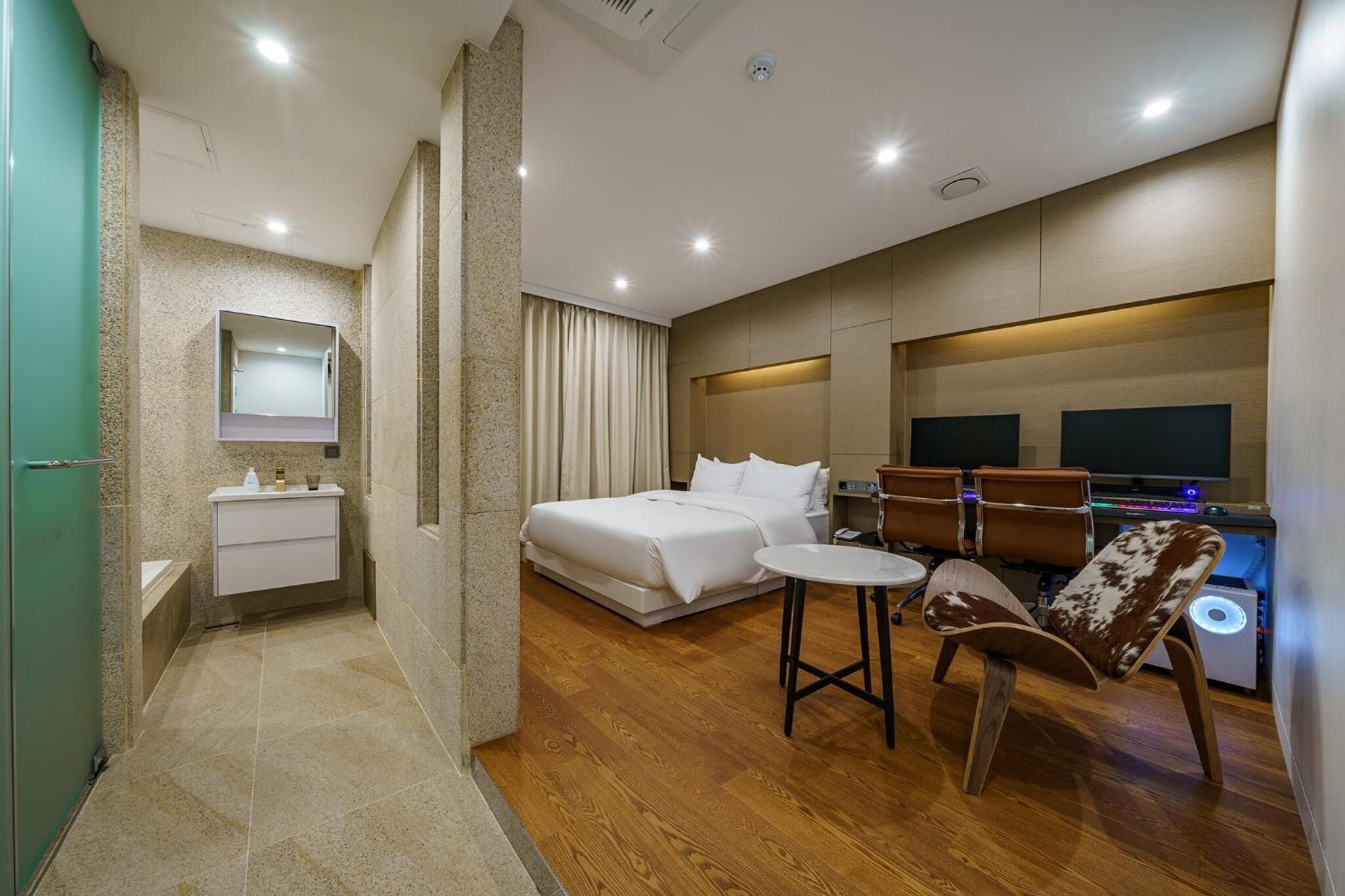 Une chambre d’hôtel moderne équipée d’un lit, d’un petit bureau, d’une chaise, d’une télévision et d’une salle de bain avec un miroir et un lavabo.