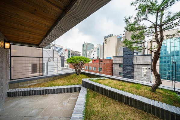 A modern urban rooftop with a wooden ceiling, a small tree, and a view of surrounding buildings. - Hotel Amare (Seoul)