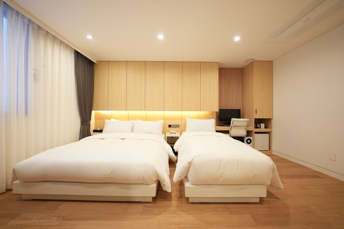 Ein modernes Hotelzimmer mit zwei Betten, einem Schreibtisch, einem Fernseher und einer kleinen Sitzecke.