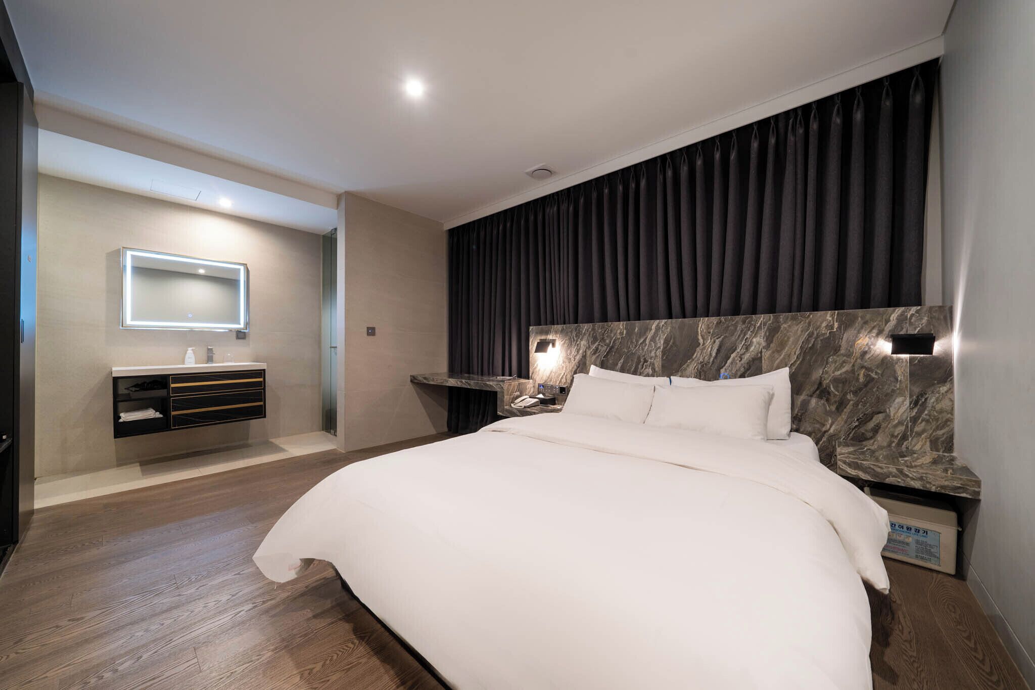 A modern hotel room with a large bed, a vanity with a mirror, and a marble headboard.
