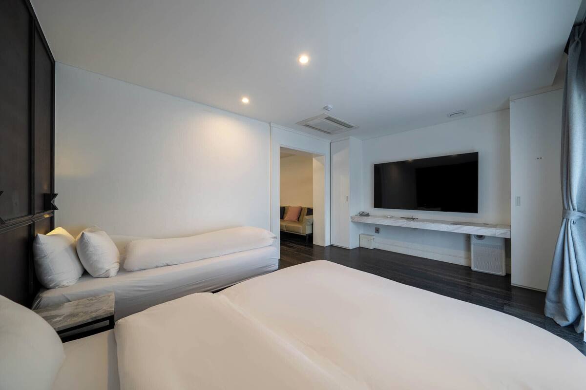 Ein modernes Hotelzimmer mit einem großen Bett, einer kleinen Sitzecke, einem flachbildfernseher an der Wand und einem begehbaren Kleiderschrank.