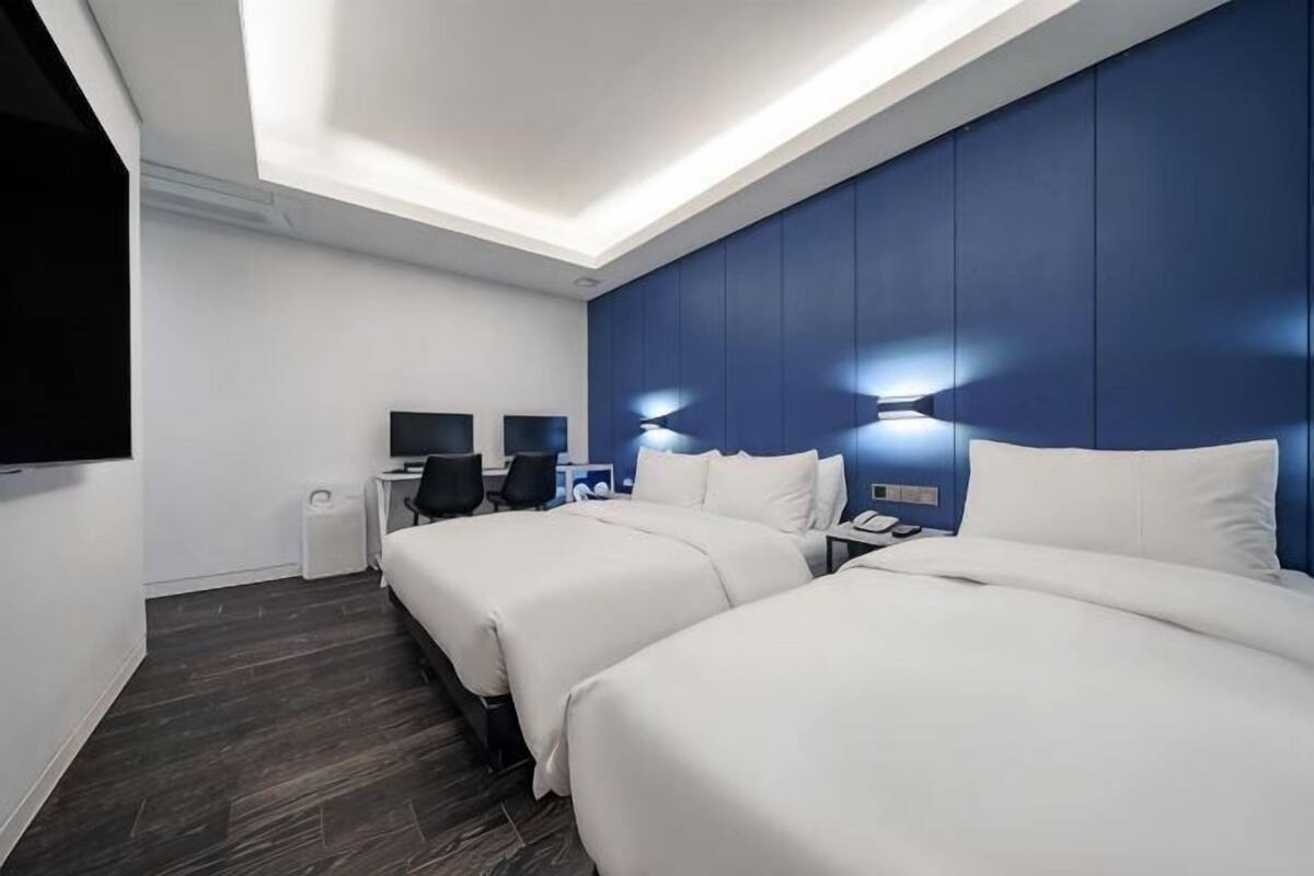Ein Hotelzimmer mit zwei Betten, einem Schreibtisch, einem Stuhl, einem Fernseher und einer Wandleuchte.
