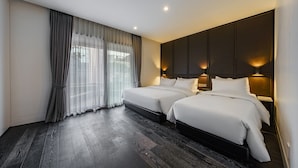 Habitación de hotel con dos camas, piso de madera oscura, ventanas amplias con cortinas translúcidas e iluminación empotrada.