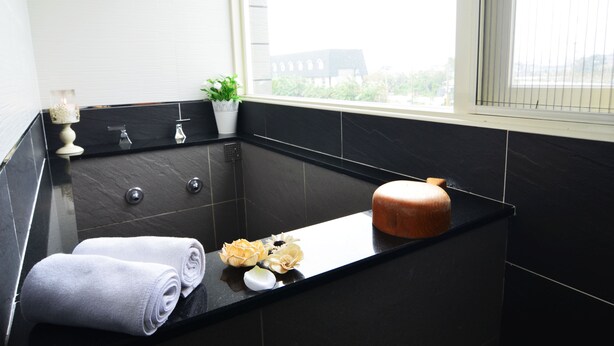 A modern bathroom with a black marble tub, two rolled towels, a potted plant, and a candle on the counter. - Yunju Hotspring Villa (Jiaoxi)