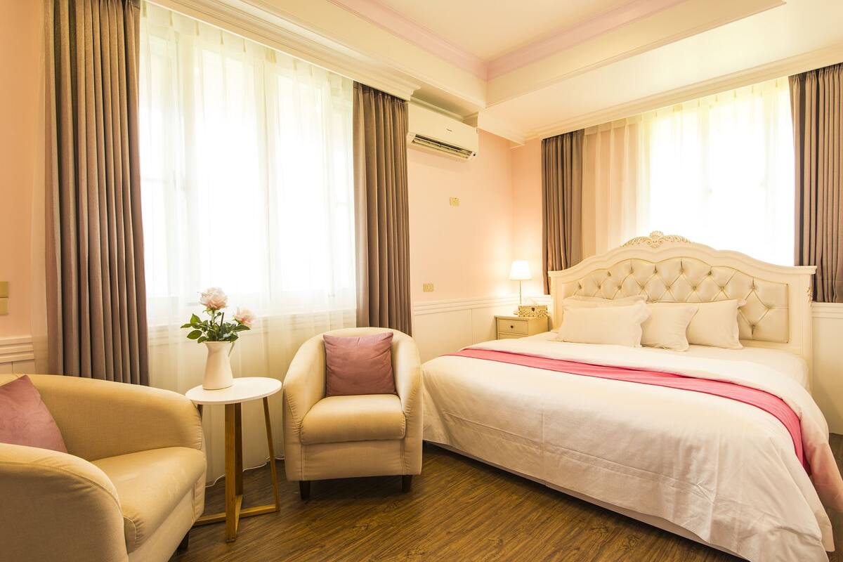 Une chambre d’hôtel avec un grand lit, un coin salon comprenant une chaise et une petite table, et une fenêtre avec des rideaux.