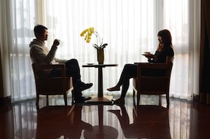 Two people seated at a small table with a vase of yellow flowers, in a room with a reflective floor and sheer curtains. - Yunju Hotspring Villa (Jiaoxi)