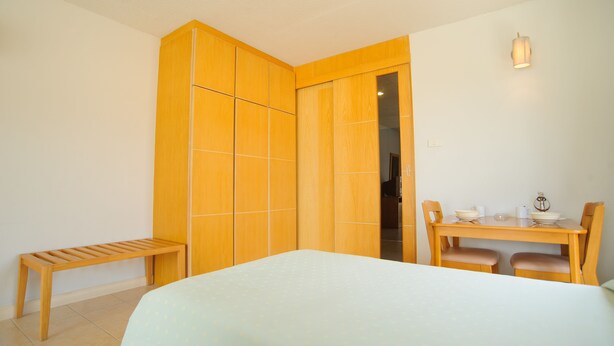 A room with a bed, a wooden bench, a dining table with chairs, and a wardrobe. - Diamond City Place (Pattaya)