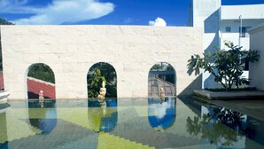 A swimming pool with clear water, three arched openings, and a white wall with a textured surface. - Diamond City Place (Pattaya)