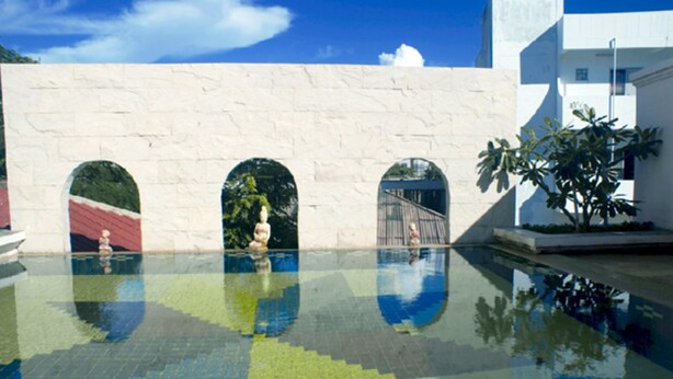 A swimming pool with clear water, three arched openings, and a white wall with a textured surface. - Diamond City Place (Pattaya)
