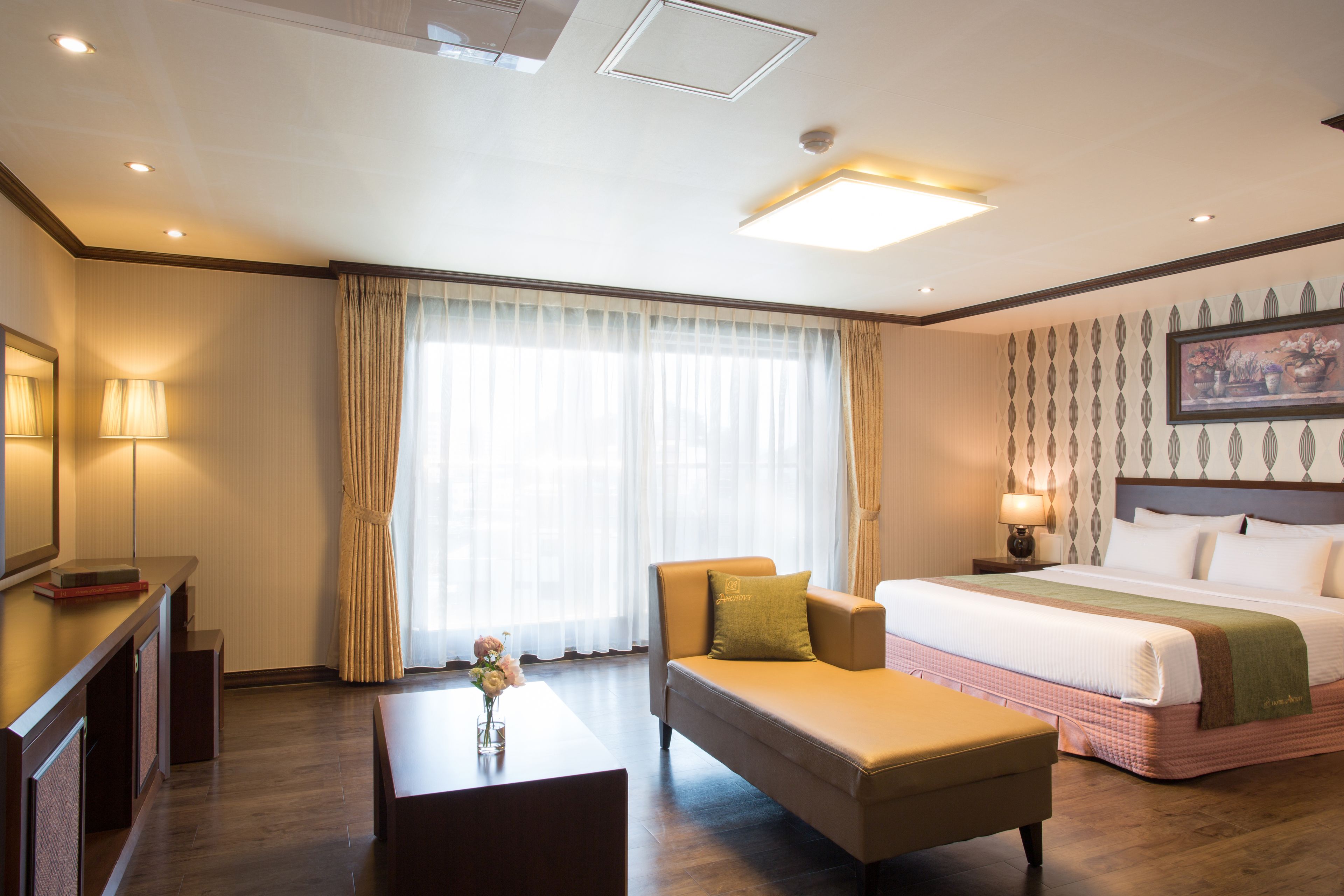 A hotel room with a bed, a sofa, a desk, and a large window with curtains.
