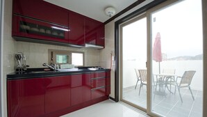 A modern kitchen with red cabinets, a black countertop, and a view of a balcony with chairs and a table. - Tongyeong Anchovy tourist Hotel (Tongyeong)