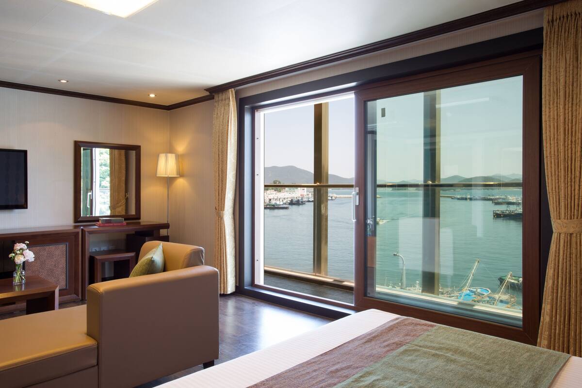 A hotel room with a large window offering a view of the water and mountains.