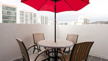 Una mesa redonda con cuatro sillas y un paraguas rojo en un patio empedrado con vistas a la ciudad.