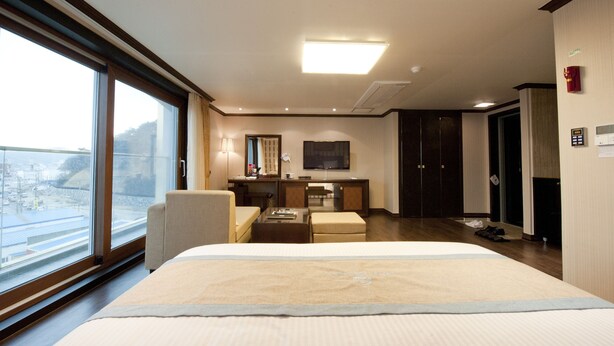 A hotel room with a large bed, a desk, a chair, and a view of the outside. - Tongyeong Anchovy tourist Hotel (Tongyeong)